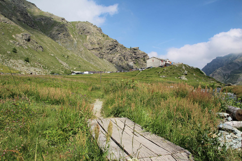 Vista della zona di Pian del Re verso valle: in primo piano la torbiera con un ponticello, sullo sfondo il rifugio e il parcheggio