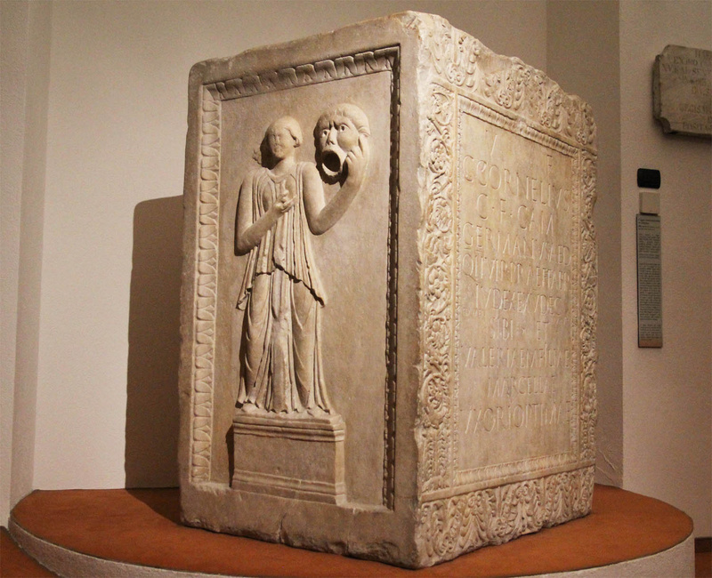 Cippo funerario in marmo con altorilievo rappresentante la musa della tragedia che regge un mascherone con la bocca aperta come in un grido