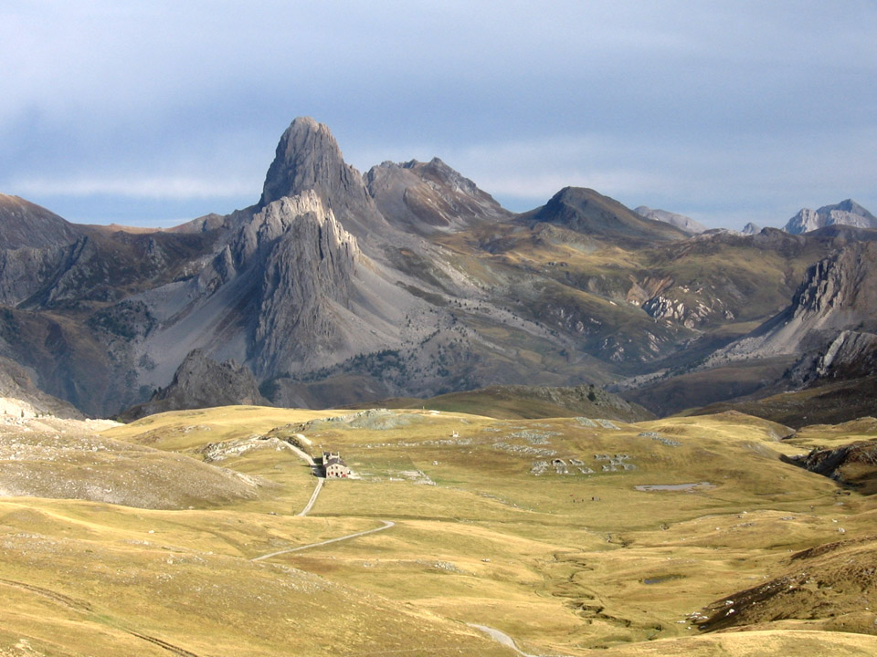 LAltopiano della Gardetta con le montagne sullo sfondo e i prati gialli autunnali in primo piano, con il rifugio al centro